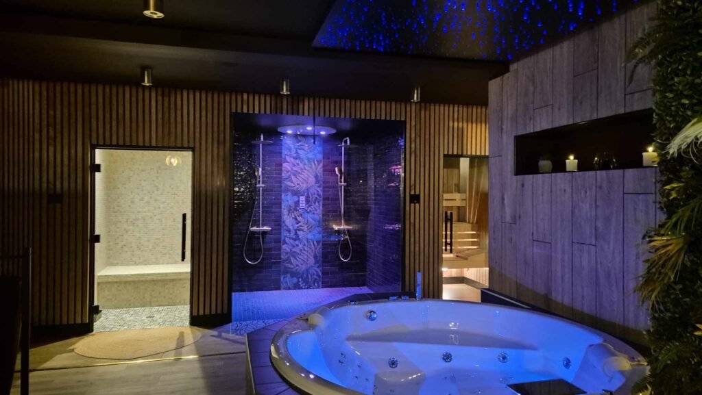 Spa privatif éclairé en rose avec bougies, ouvert sur la suite cocooning et végétalisée de la Love Room Toi & Moi à Chartres